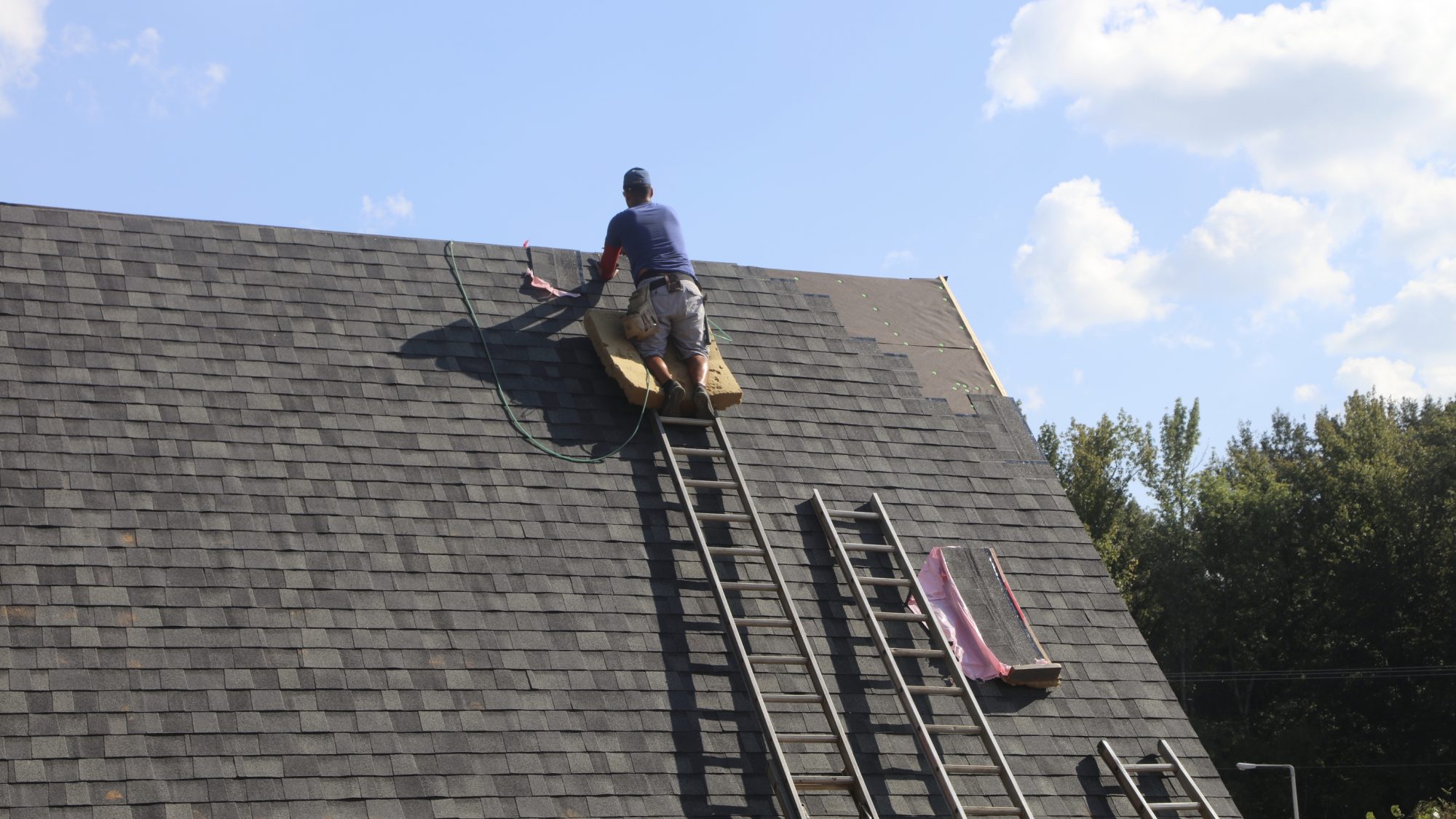 A roofer in the process of installing a roof on a new construction house.